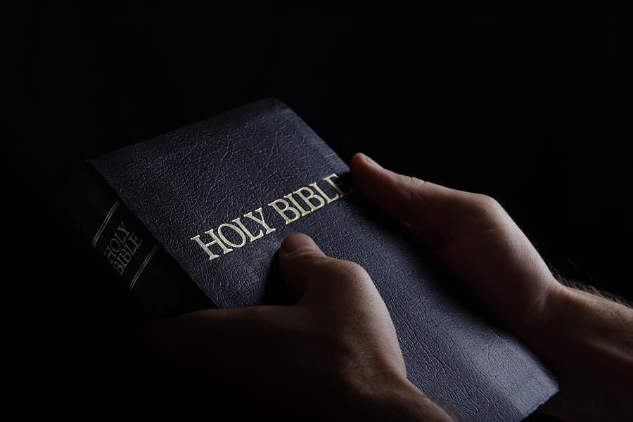 Man holding the Holy Bible in a dark setting Photograph by Rmfox