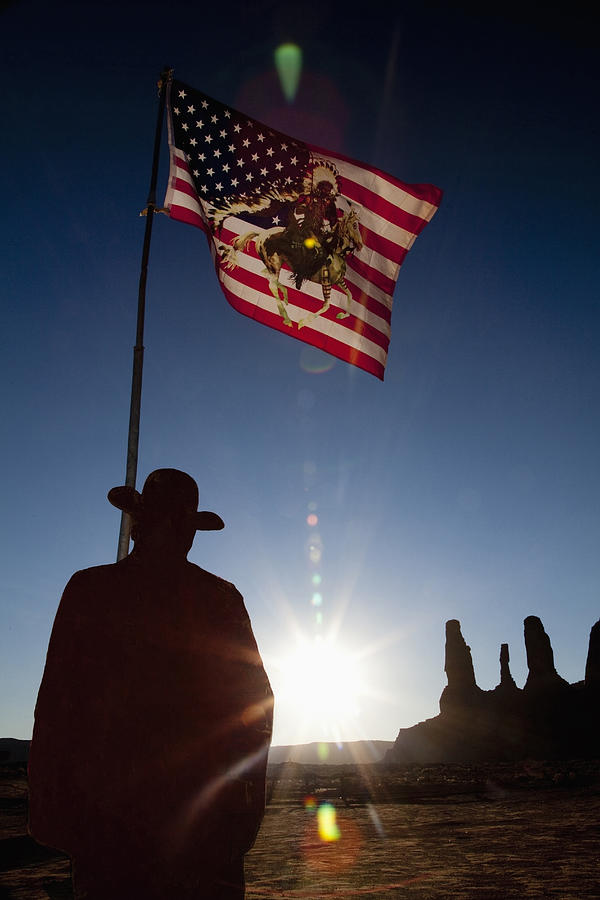Man holding United States flag with Native American depiction near rock formations, Monument Valley, Utah, United States Photograph by Camilo Morales