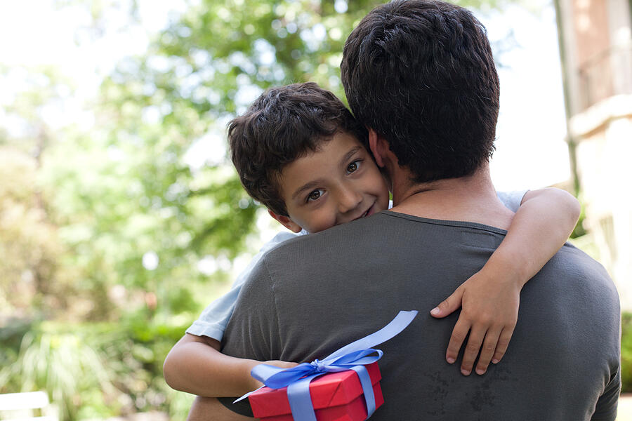 Man hugging smiling young boy holding gift outdoors Photograph by Sam Edwards
