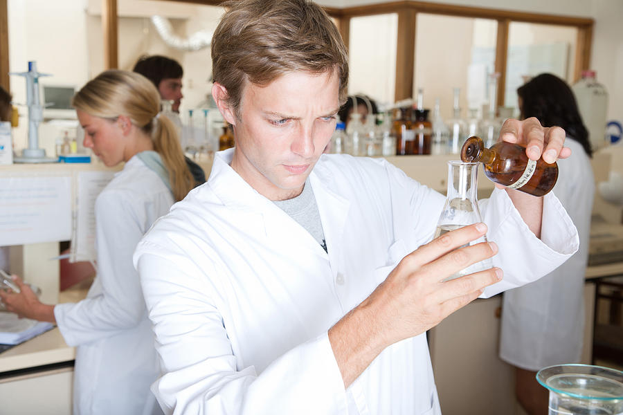 Man in a busy laboratory measuring liquids Photograph by Paul Bradbury