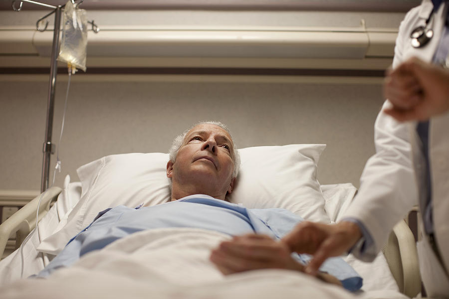 Man in hospital bed having pulse taken Photograph by David Sacks