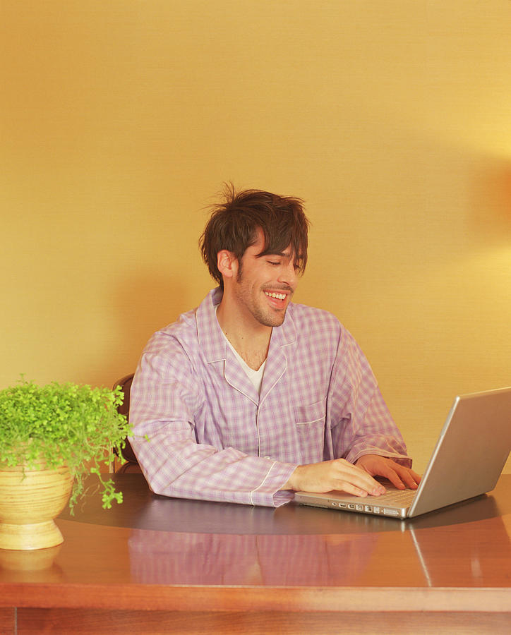 Man in pajamas using laptop computer Photograph by Jupiterimages
