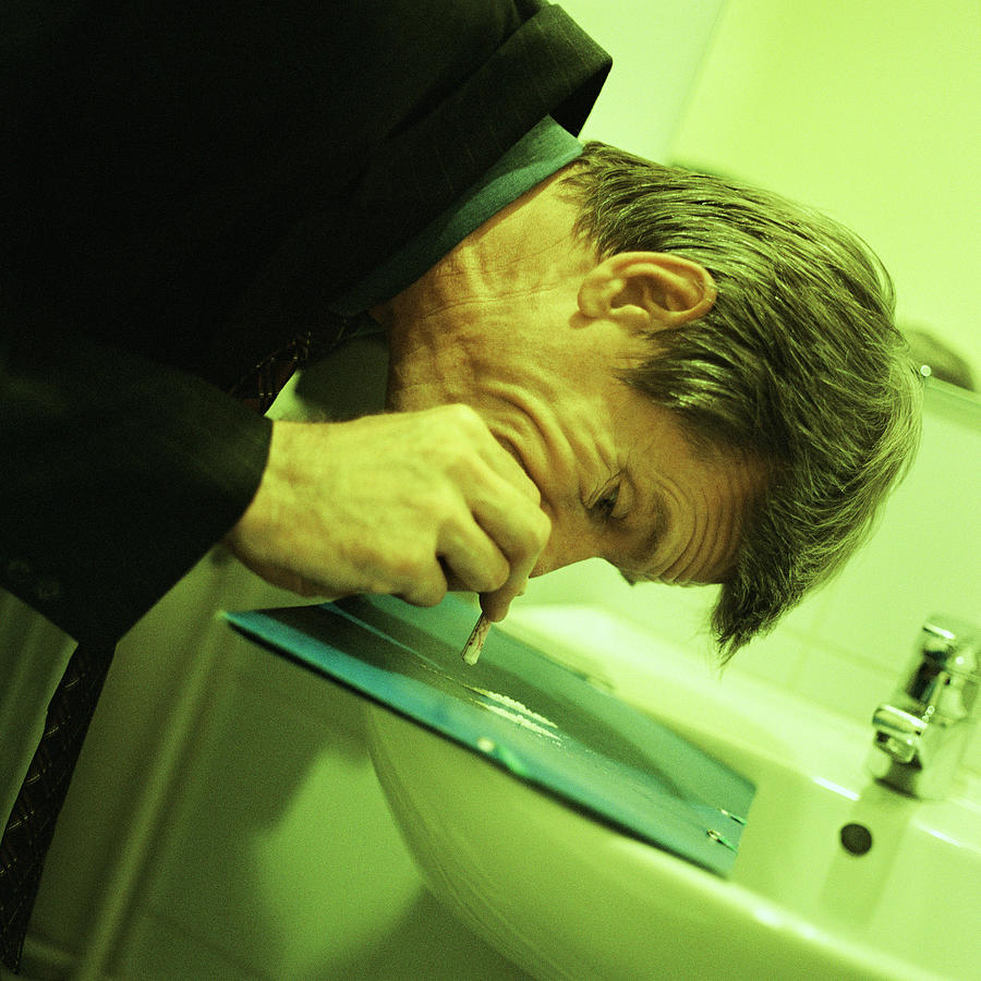 Man in suit snorting cocaine in bathroom. Photograph by Patrick Sheandell OCarroll