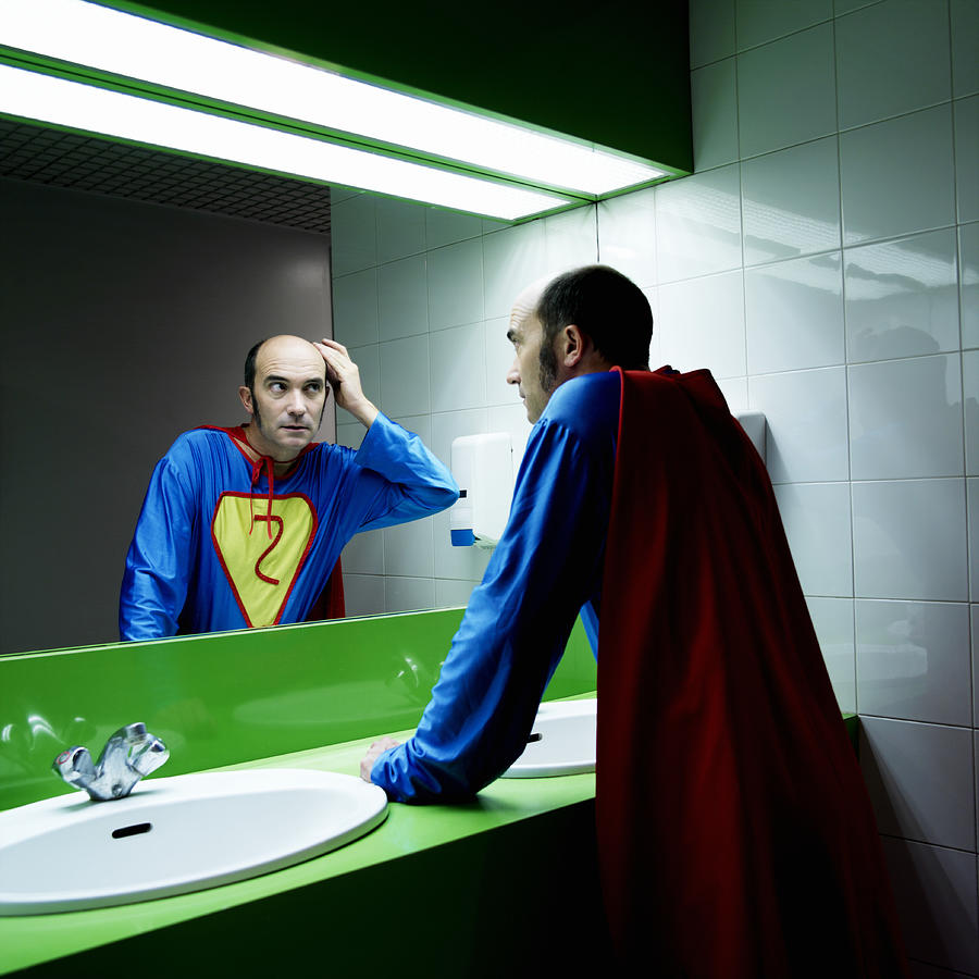 Man in superhero costume looking at reflection in mirror Photograph by Roger Wright