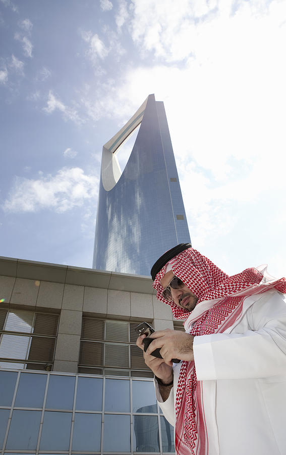 Man in Thobe using mobile phone, Kingdom Tower, Riyadh, Saudi Arabia Photograph by Tim E White