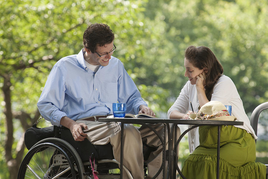 Man in wheelchair with spinal cord injury reading a book at cafe with his pregnant wife Photograph by Huntstock