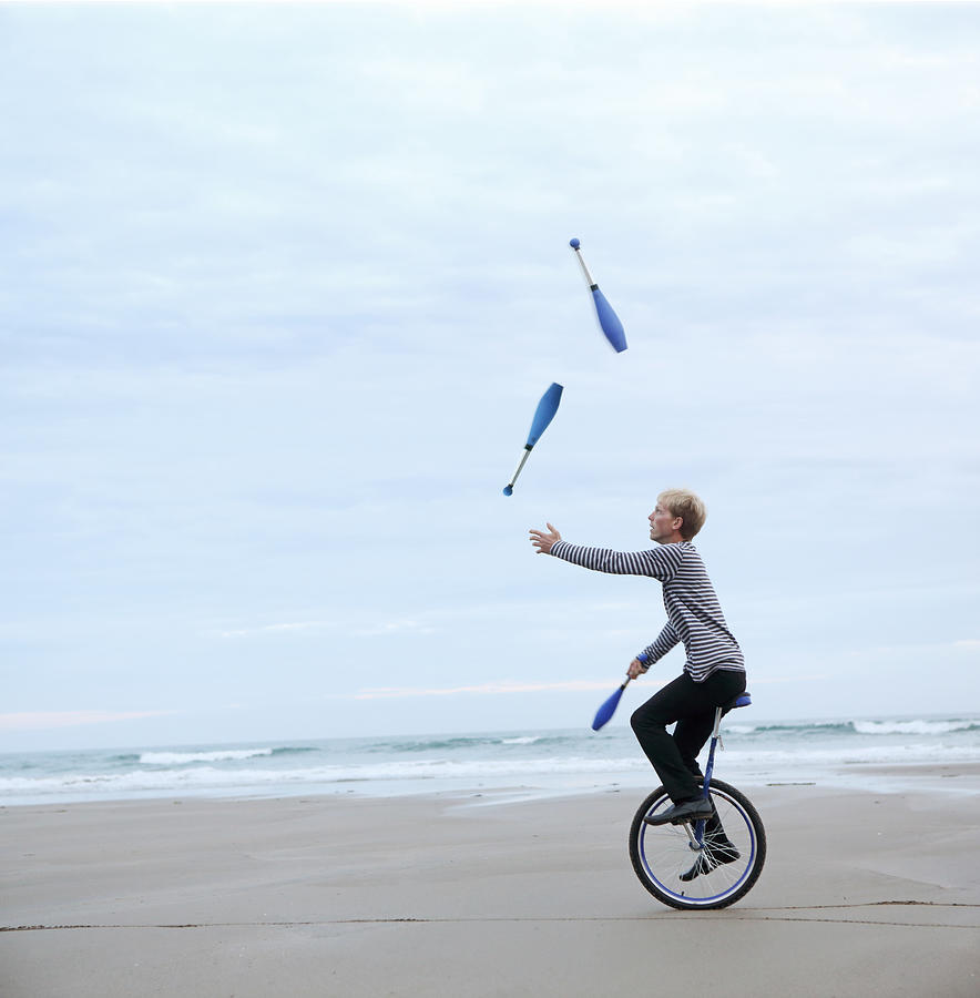 Man juggling pins on unicycle on beach Photograph by Peter Cade