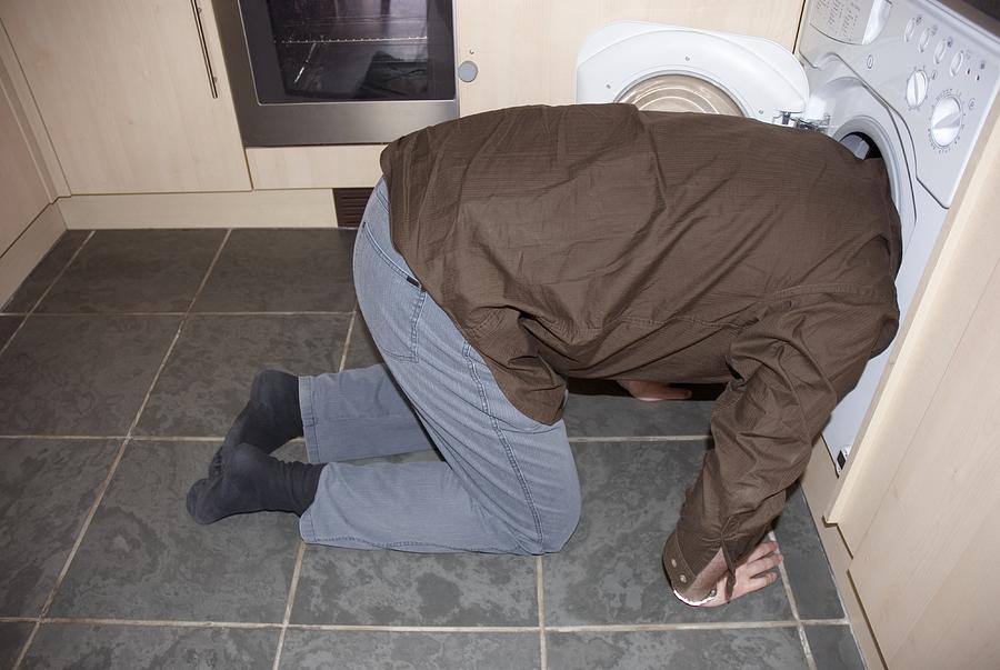 Man kneeling down with his head in a washing machine Photograph by Martin Holtkamp