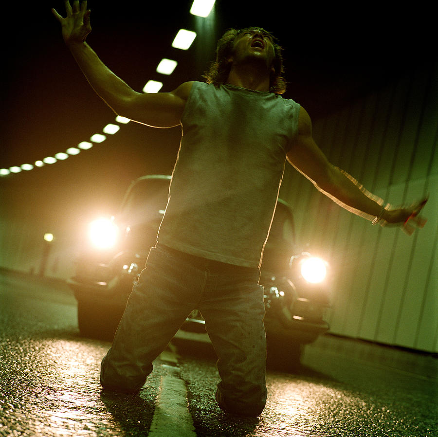 Man kneeling on road in front of car, arms outstretched, close-up Photograph by Frank Herholdt