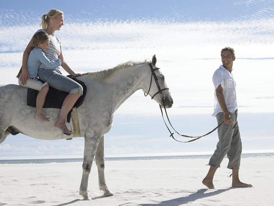 Man Leads a Horse With His Wife and Daughter Along the Beach Photograph by Digital Vision.