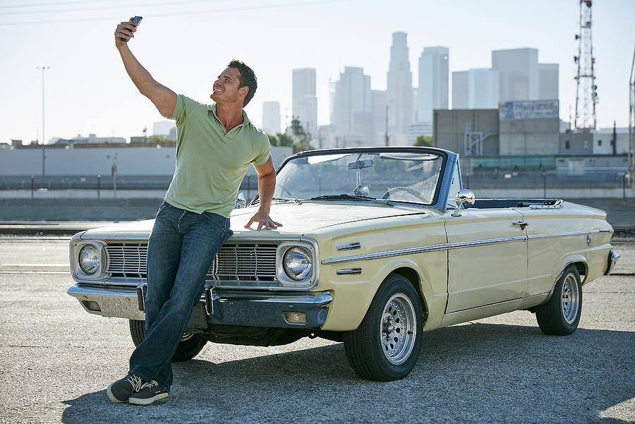 Man leaning against convertible car taking selfie, Los Angeles, California, USA Photograph by Tony Garcia