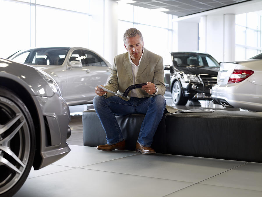 Man looking at brochure in automobile showroom Photograph by Adam Gault