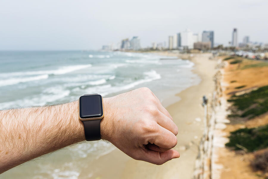 Man looking at his smart watch on the beach with city skyline in the background Photograph by Alexander Spatari