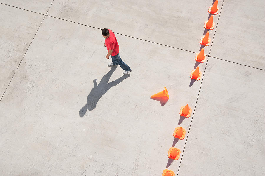 Man looking at row of traffic cones with one misplaced Photograph by Martin Barraud
