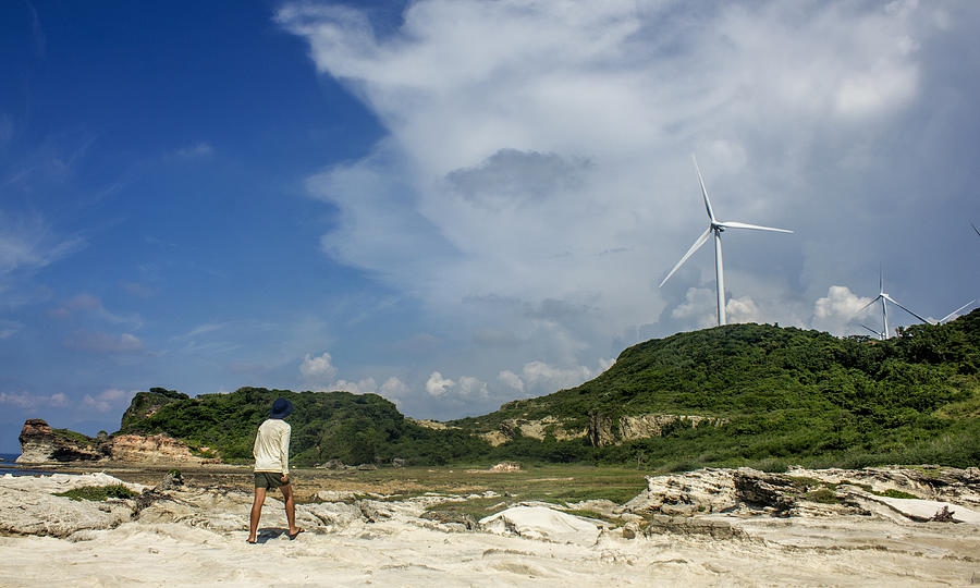 Man looking at the windmills at Kapurpurawan Rock Formation Photograph by Chris Dela Cruz