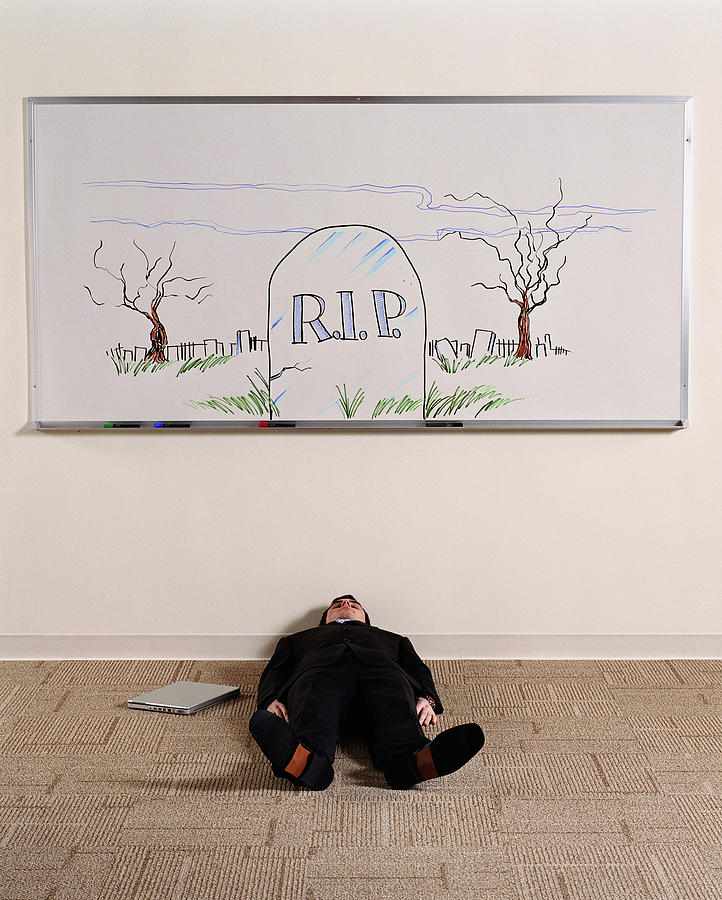 Man lying on floor under whiteboard illustrated with grave stone Photograph by Ryan McVay