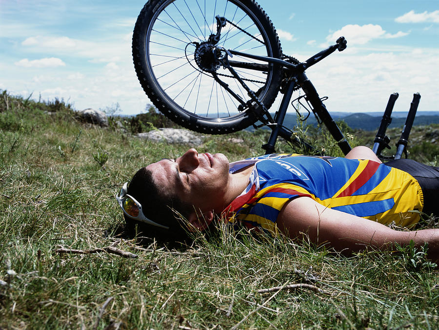 Man lying on grass beside mountain bicycle, side view Photograph by Hans Neleman