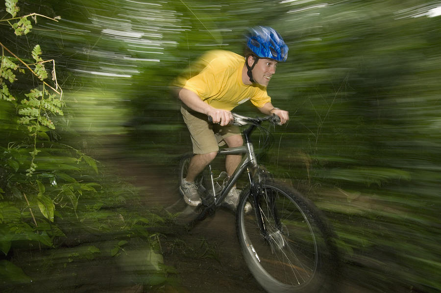 Man mountain biking in forest, (blurred motion) Photograph by Kevin Schafer
