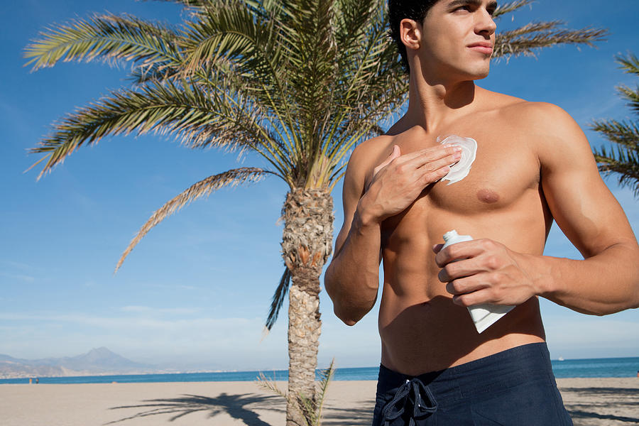 Man on a beach applying sunblock lotion to himself Photograph by Chris Ryan