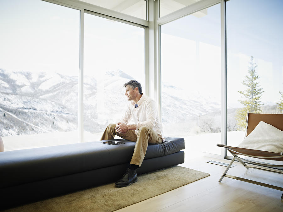 Man on couch in modern home with digital tablet Photograph by Thomas Barwick