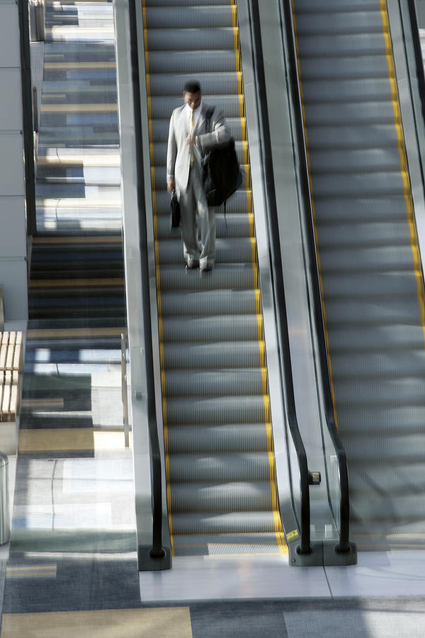 Man on escalator with luggage Photograph by Comstock Images