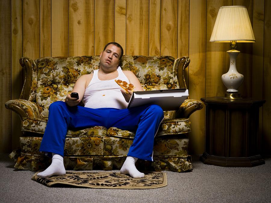 Man on sofa with pizza and TV remote Photograph by Rubberball/Mike Kemp