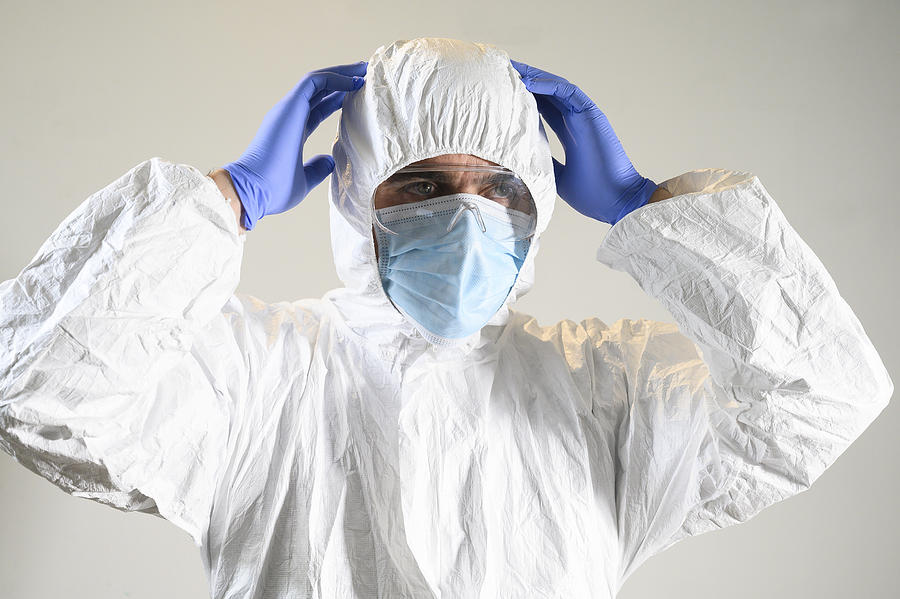 Man or scientist with mask with hands up on his head, gloves and protective suit (hazmat suit). White background. Coronavirus and other viruses and their Analysis. Photograph by Aitor Diago