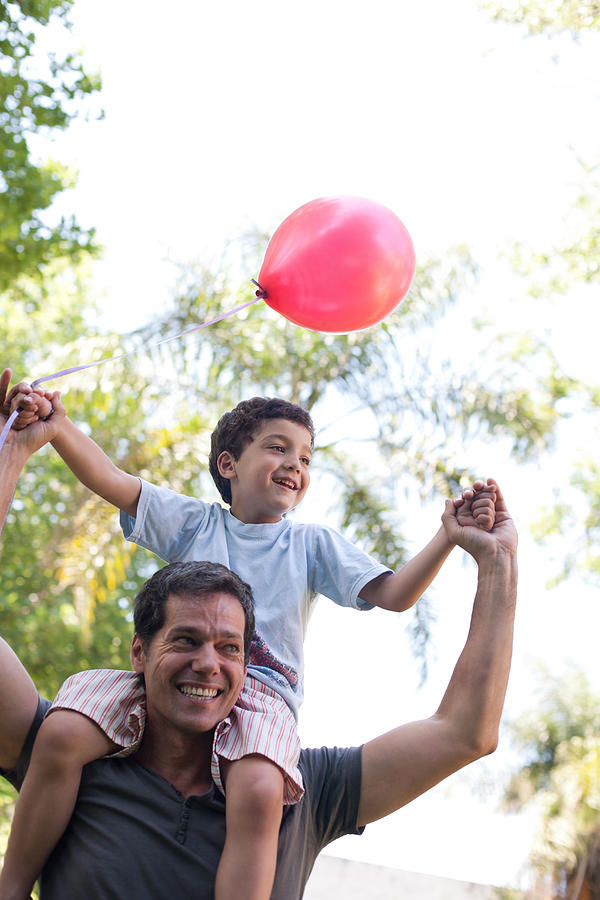 Man outdoors giving smiling young boy shoulder ride with balloon Photograph by Sam Edwards