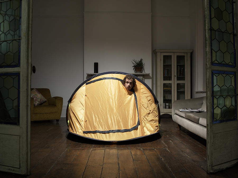 Man peering from tent in living room Photograph by Simon Bremner