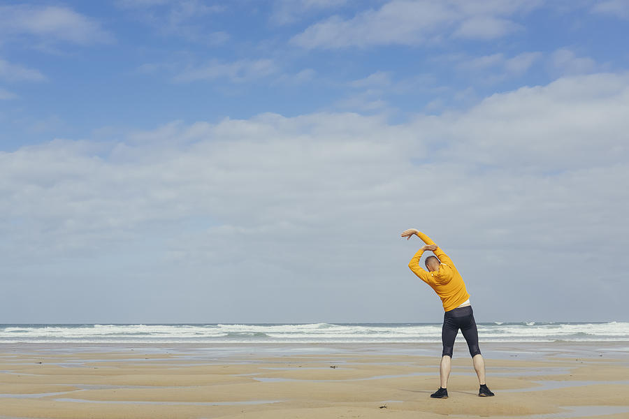 Man performing warm up exercises before moving beach run. Photograph by Creacart