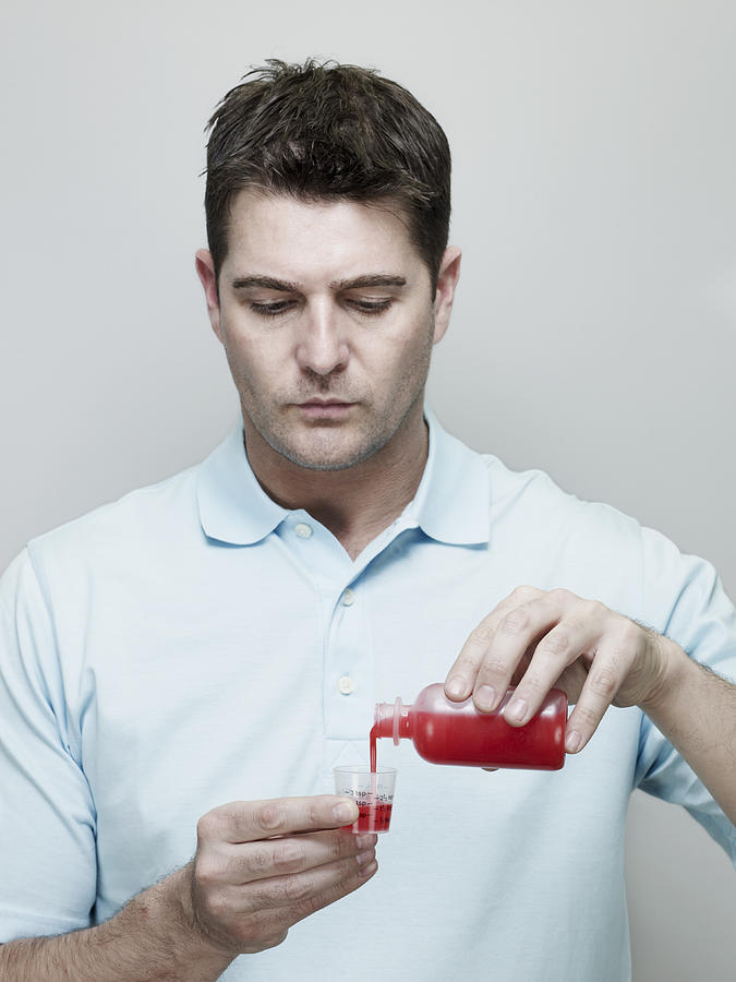 Man Pouring Cough Medicine into Measuring Cup. Photograph by Ballyscanlon