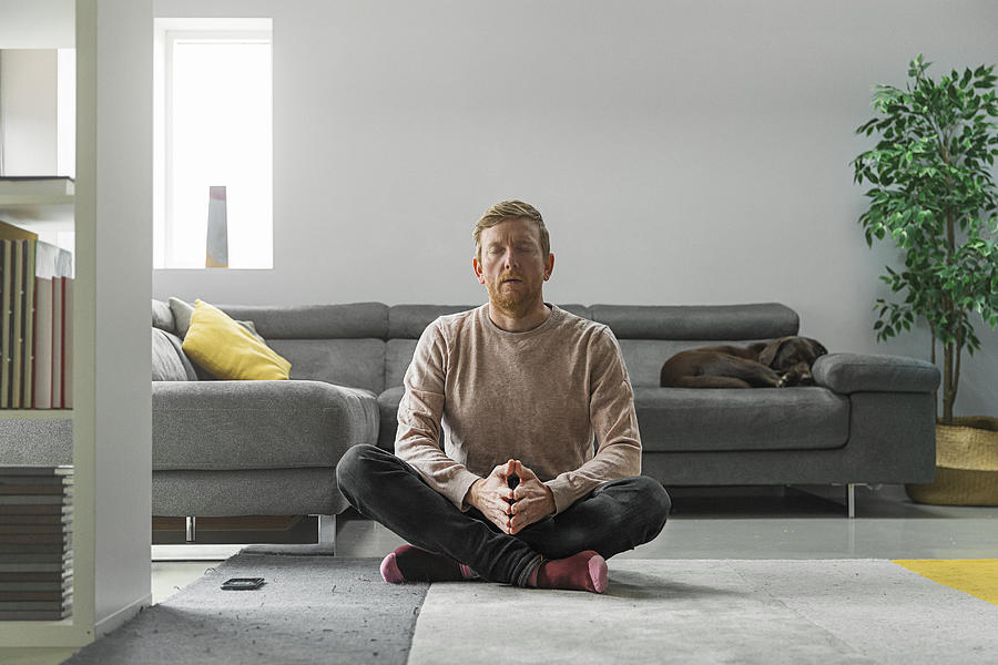 Man practising meditation in living room Photograph by Justin Paget
