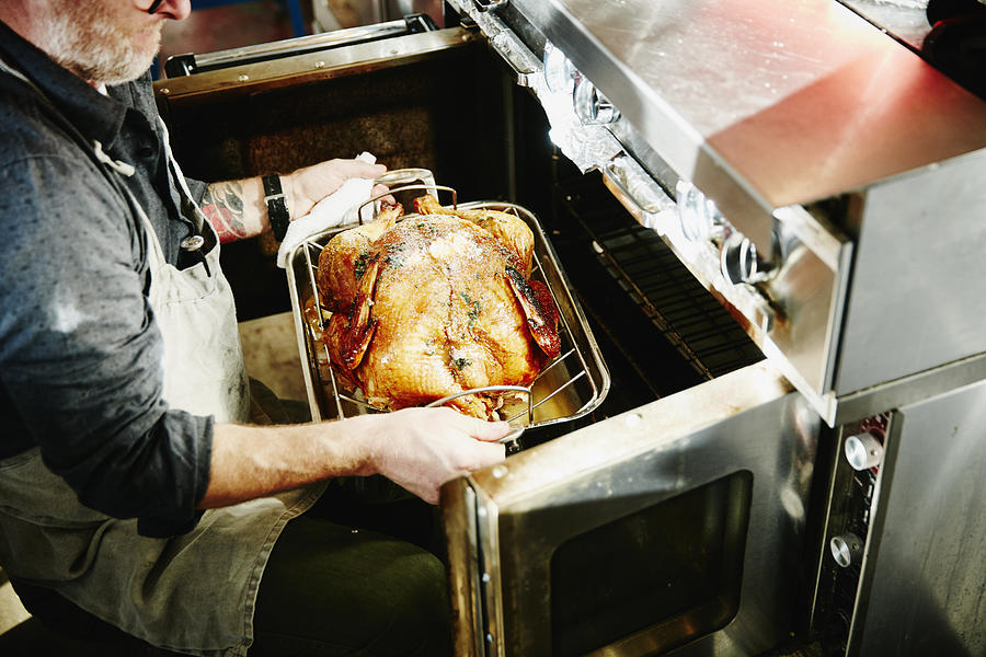Man pulling cooked turkey out of oven Photograph by Thomas Barwick