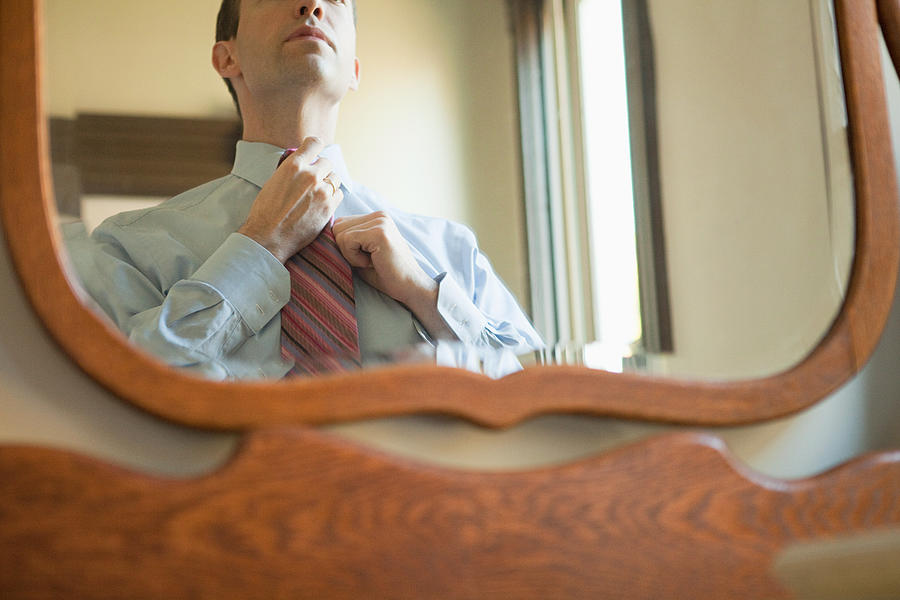 Man putting on tie in mirror Photograph by Image Source
