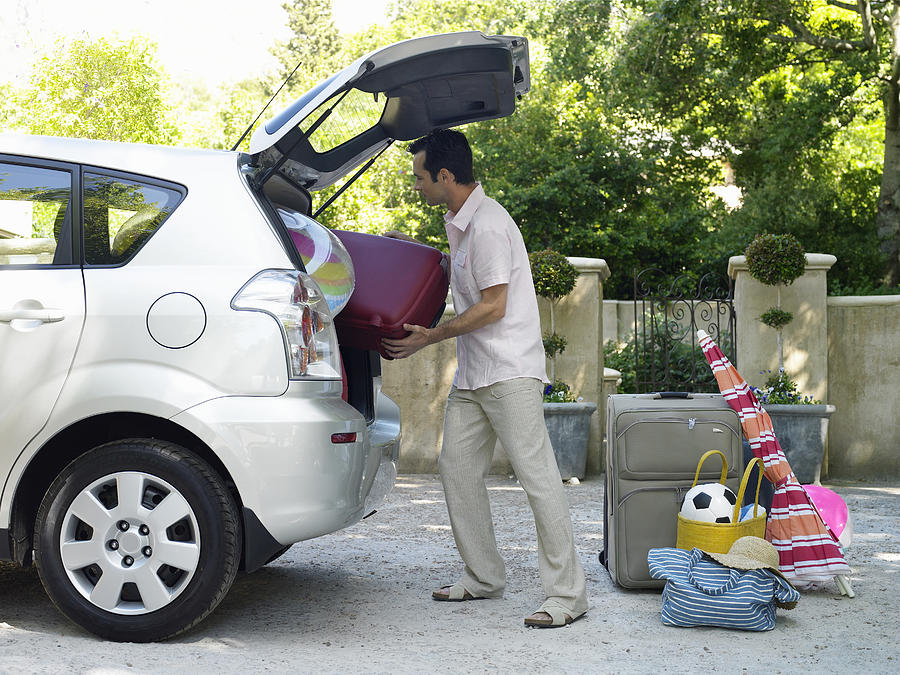 Man putting suitcases into boot of car, side view Photograph by Flying Colours Ltd