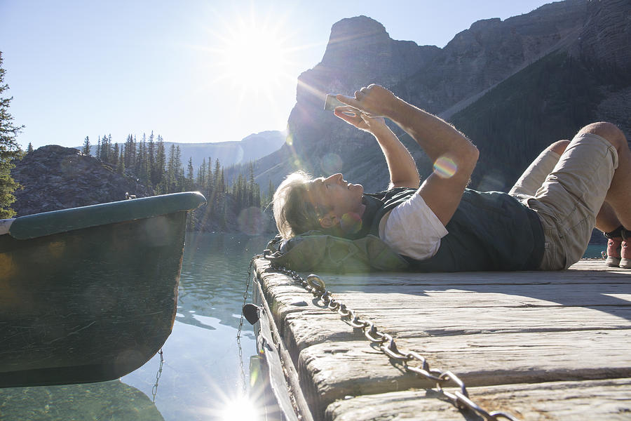 Man relaxes by canoe at dock, uses digital tablet Photograph by Ascent/PKS Media Inc.