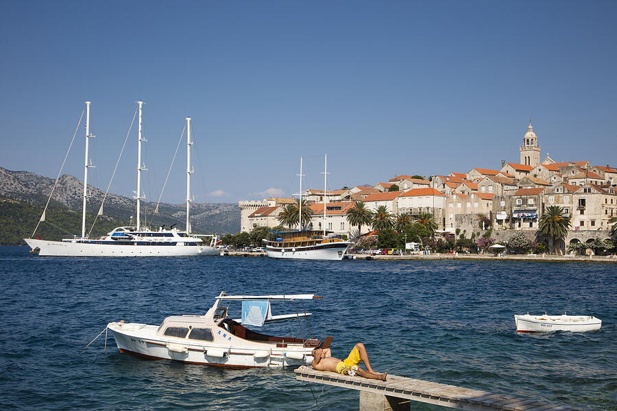 Man relaxes on jetty with Korcula Old Town behind Photograph by Holger Leue