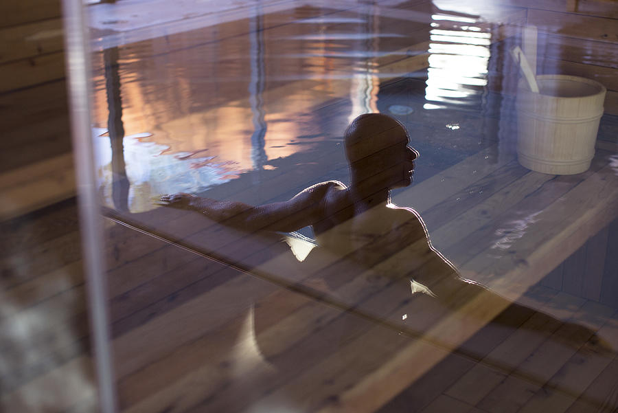 Man relaxing in swimming pool, reflected on glass door Photograph by PhotoAlto/Anne-Sophie Bost
