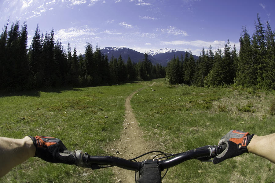 Man riding mountain bike on dirt footpath, mountains in background Photograph by Darryl Leniuk