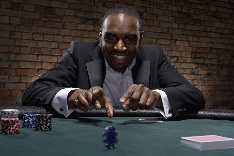 Man rolling poker chip in casino Photograph by Duncan Nicholls and Simon Webb