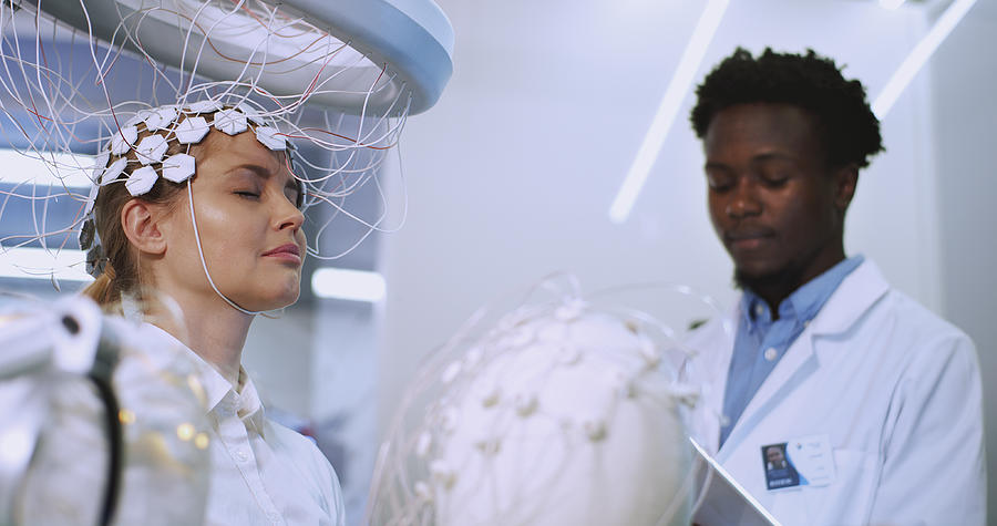 Man Scientist examining womans brain by Brainwave Scanning Headset in laboratory. Photograph by Slavemotion