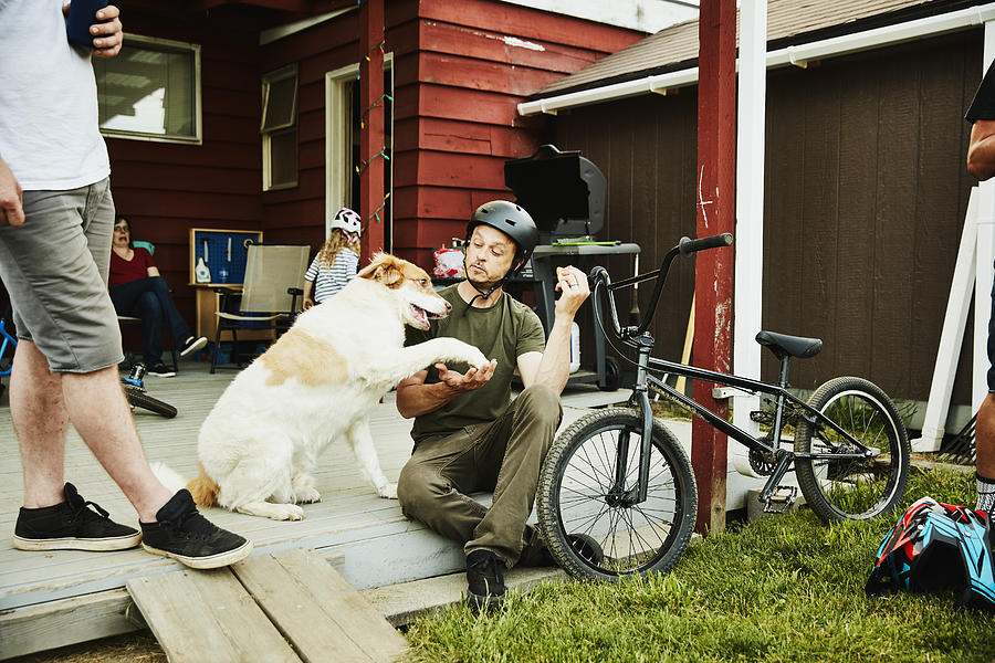 Man shaking hands with dog with eating hot dog on back porch with friends on summer evening Photograph by Thomas Barwick