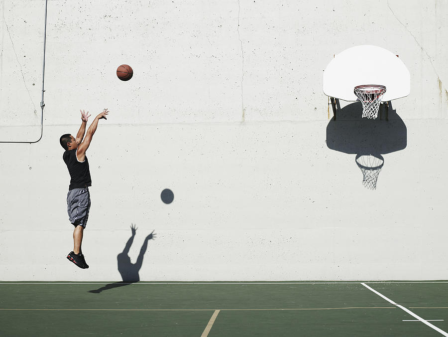 Man shooting jump shot on outdoor basketball court, side view Photograph by Thomas Barwick