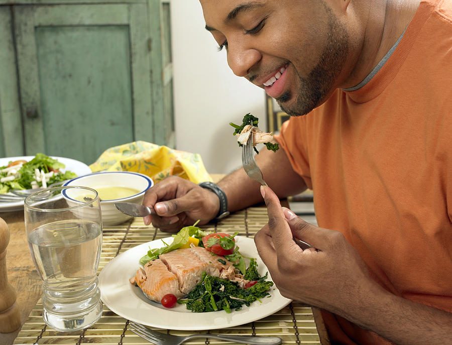 Man Sits at a Table at Home Eating a Salmon Salad for Lunch Photograph by Digital Vision.