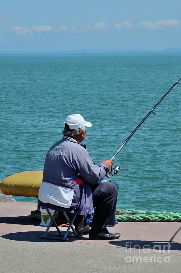 Man sits by Black sea shore with fishing pole Batumi Georgia Photograph by Imran Ahmed