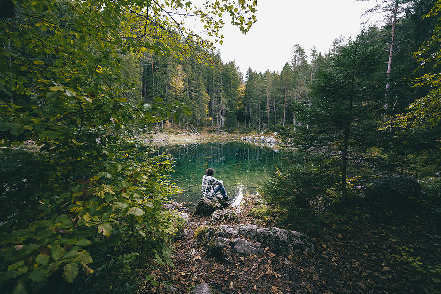 Man sitting admiring an emerald lake in the forest Photograph by © Marco Bottigelli