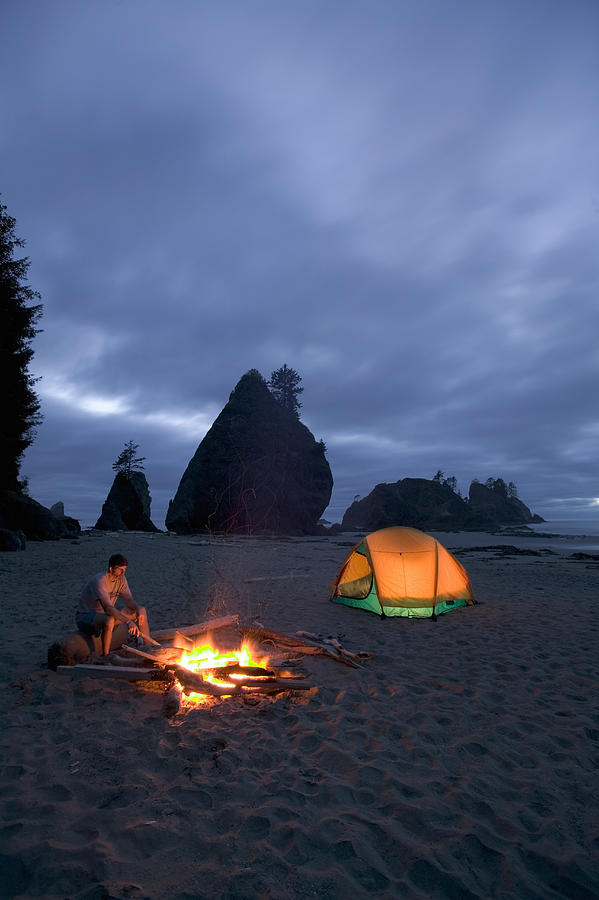 Man sitting by campfire on beach, night Photograph by Rene Frederick