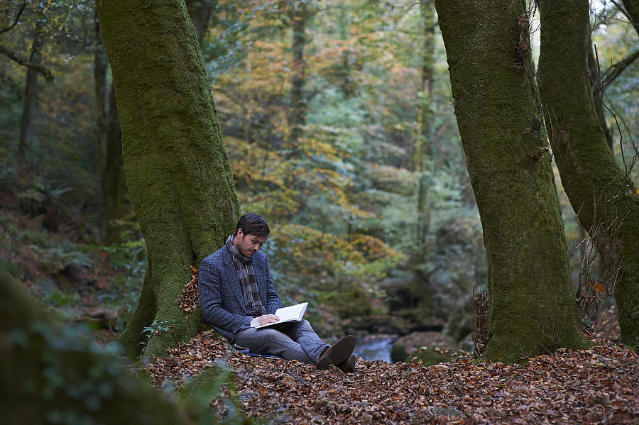 Man sitting in Autumn woodland reading book. Photograph by Dougal Waters