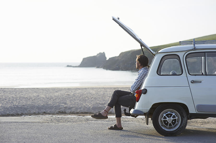 Man sitting in boot of retro car at beach. Photograph by Dougal Waters