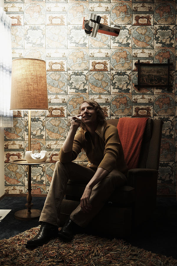 Man sitting in chair in room, talking on phone Photograph by Thomas Northcut